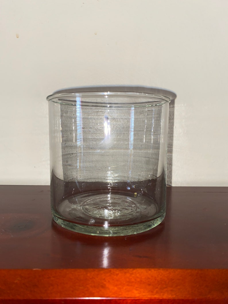 K&ouml;nnte beinhalten: Ein klarer, zylindrischer Glasbeh&auml;lter mit einer weiten &Ouml;ffnung. Der Beh&auml;lter besteht aus transparentem Glas und steht auf einer dunklen Holzoberfl&auml;che. Der Beh&auml;lter ist leer und scheint ein dekorativer oder Aufbewahrungsbeh&auml;lter zu sein.