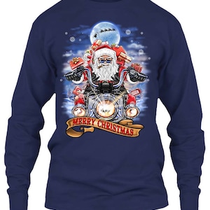 May include: Navy blue long-sleeve shirt featuring a graphic of Santa Claus riding a motorcycle, carrying gifts. The design includes a full moon, snowflakes, and the text "MERRY CHRISTMAS" on a banner. The shirt is a festive holiday item.