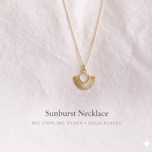 May include: A gold-plated 925 sterling silver necklace featuring a sunburst pendant. The pendant consists of a central circular ring with radiating rays extending from the bottom half. The text Sunburst Necklace 925 STERLING SILVER GOLD-PLATED is visible.