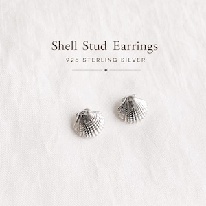 May include: A pair of 925 sterling silver shell stud earrings with a textured, fan-shaped design. The text Shell Stud Earrings 925 STERLING SILVER is printed above the earrings, which feature a metallic finish and detailed ridges.