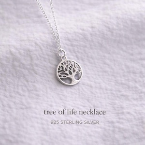 May include: A silver necklace featuring a circular pendant with a cut-out tree of life design. The pendant hangs from a delicate silver chain. The text tree of life necklace and 925 STERLING SILVER is printed below the pendant.