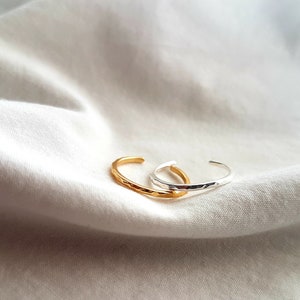 Peut inclure: Deux anneaux en métal martelé, l'un en or et l'autre en argent, sur un fond de tissu blanc.