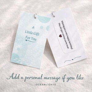 May include: Two white gift tags with silver metal loops. One tag reads "A Little Gift For You" with blue watercolor accents. The other tag has a birthday message and a heart. The text "Add a personal message if you like" is below.