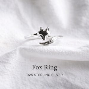 Könnte beinhalten: Ein silberner Fuch-Ring mit detailliertem Fuchs-Kopf und Schwanz-Design. Der Ring besteht aus 925er Sterlingsilber und wird auf weißem Hintergrund präsentiert. Der Text "Fox Ring" und "925 STERLING SILVER" ist sichtbar.