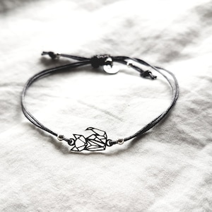 May include: A black cord bracelet featuring a central geometric fox charm made of thin black metal lines. The bracelet includes two small silver-toned metal beads flanking the fox charm and a small circular metal tag near the adjustable knot closure.