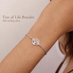 Op de afbeelding: Een Levensboom-armband met een ronde 925 sterling zilveren bedel met een gedetailleerd boomontwerp, bevestigd aan een dun, lichtgrijs koord. De tekst Tree of Life Bracelet 925 sterling silver is zichtbaar in de linkerbovenhoek.