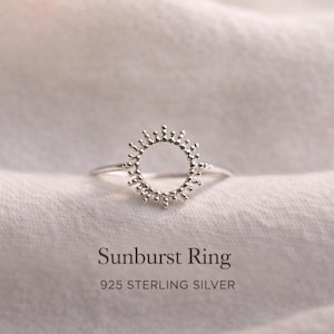 Könnte beinhalten: Ein Ring aus Sterlingsilber mit Sonnenmuster. Der Ring hat ein kreisförmiges Design mit kleinen, perlenartigen Details am äußeren Rand, die Sonnenstrahlen ähneln. Der Text "Sunburst Ring" und "925 STERLING SILVER" stehen darunter.