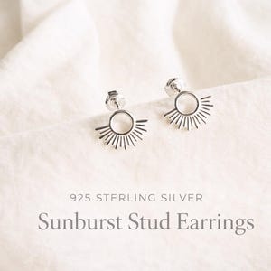 May include: A pair of 925 sterling silver stud earrings featuring a circular center with radiating sunburst rays. The text 925 STERLING SILVER Sunburst Stud Earrings is printed below the earrings in a clear, dark grey sans-serif font.