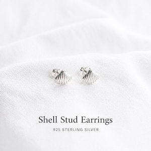 Può includere: Un paio di orecchini a lobo in argento a forma di piccole conchiglie. Gli orecchini presentano una texture a coste e sono realizzati in argento sterling 925. Il testo Shell Stud Earrings 925 STERLING SILVER è stampato sotto gli orecchini.