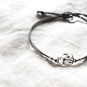 May include: A black cord bracelet featuring a silver-toned geometric fox charm. The bracelet includes small silver beads on either side of the charm and a sliding knot closure with a small circular metal tag attached near the adjustable cord ends.