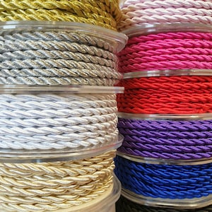 May include: A stack of spools of colourful braided cord. The cords are in various colours, including gold, silver, white, red, purple, blue, and black.