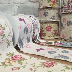 May include: A collection of fabric ribbon rolls with various floral and butterfly patterns. The ribbon is beige with pink, purple, and gray accents.