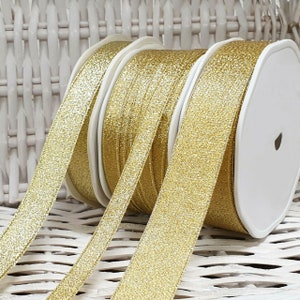 May include: Three spools of gold glitter ribbon. The ribbon is a light gold colour with a shimmery finish.