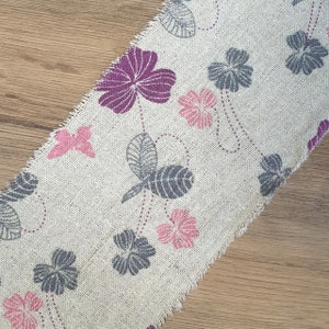 May include: A beige fabric with a floral pattern. The fabric features pink, purple, and gray flowers and butterflies.