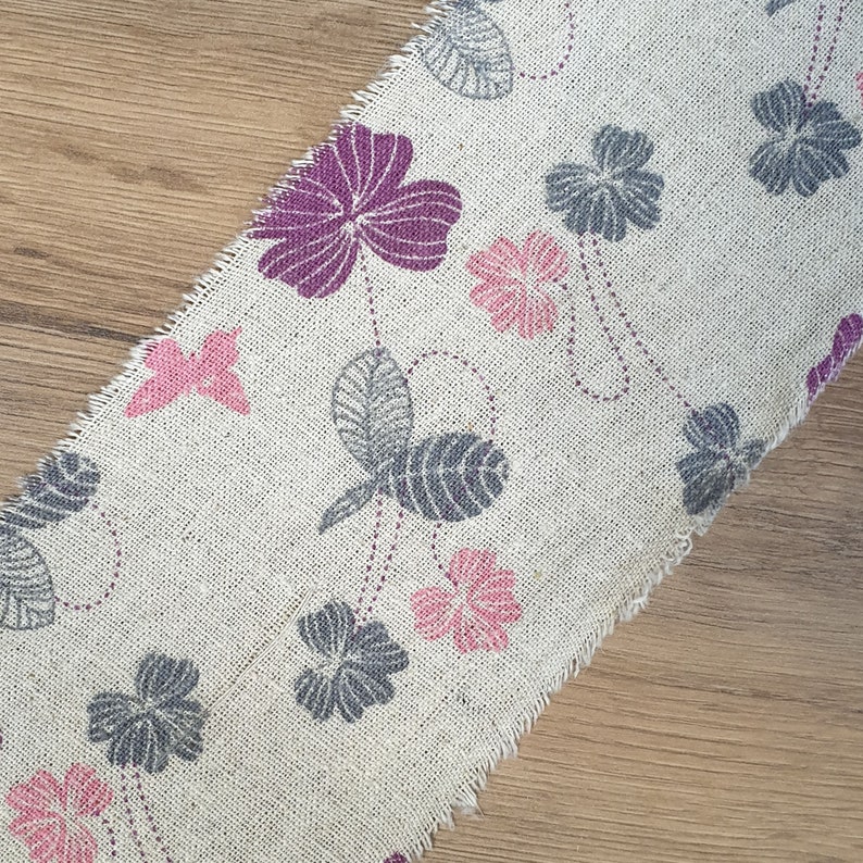 May include: A beige fabric with a floral pattern. The fabric features pink, purple, and gray flowers and butterflies.