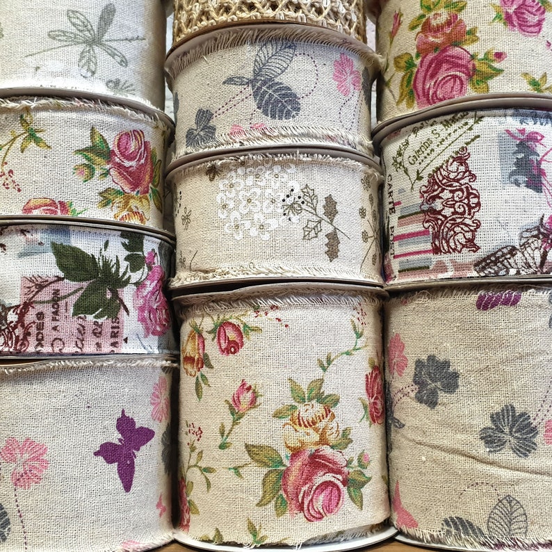 May include: A collection of spools of beige fabric ribbon with various floral and butterfly patterns. The ribbon is trimmed with a frayed edge.
