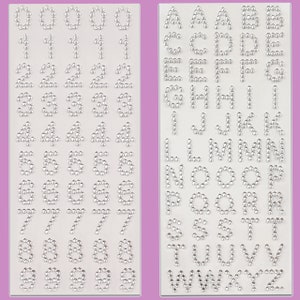 May include: Two sheets of self-adhesive rhinestones, one with the numbers 0-9 and the other with the letters A-Z. The rhinestones are silver and have a round shape.