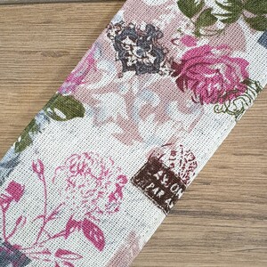 May include: A white fabric with a pink and green floral pattern. The fabric has a textured surface and a vintage look. The fabric has the text "AVION DEPART A PARIS" printed on it.