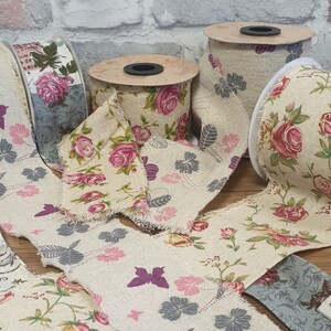 May include: Assortment of floral patterned fabric ribbon rolls. The ribbon is beige with a floral pattern in shades of pink, red, and gray. The ribbon is frayed on the edges.