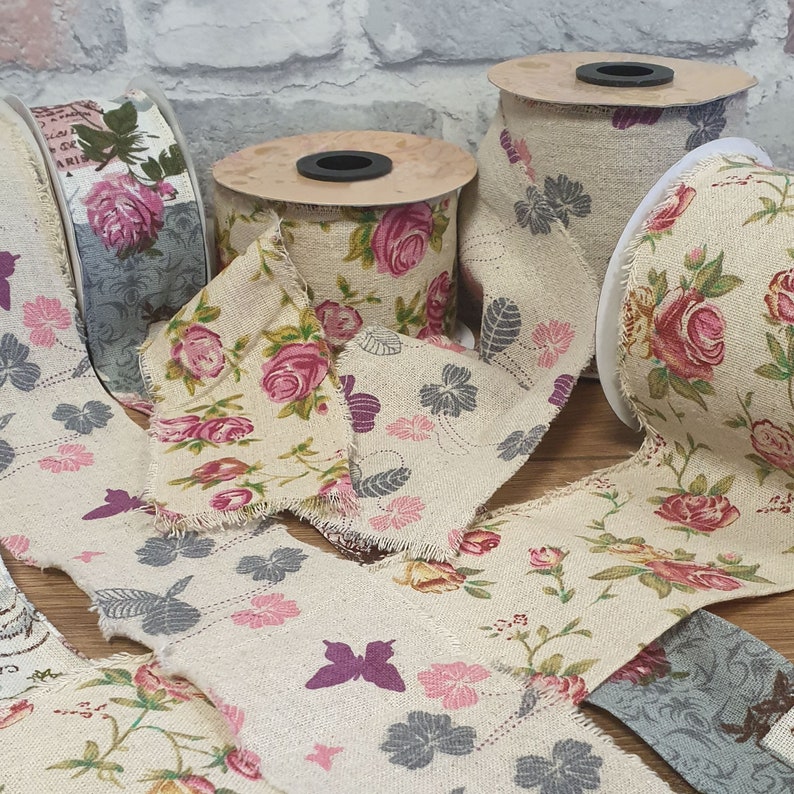 May include: Assortment of floral patterned fabric ribbon rolls. The ribbon is beige with a floral pattern in shades of pink, red, and gray. The ribbon is frayed on the edges.