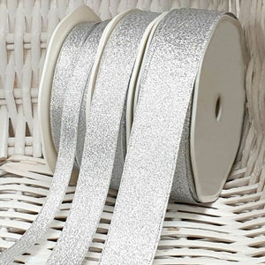 May include: Three spools of silver glitter ribbon. The ribbon is a light silver color with a subtle sparkle.