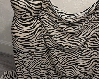 May include: Black and white zebra print fabric with a ribbed texture. The fabric is draped over a mannequin and has a soft, flowing look.