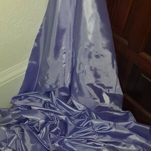 May include: A large piece of light purple satin fabric, folded and draped on a surface. The fabric has a smooth, shiny texture.