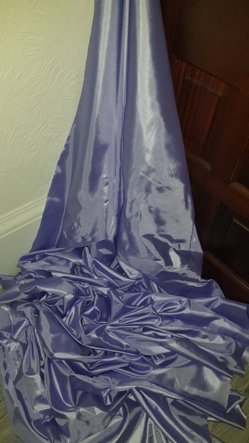 May include: A large piece of light purple satin fabric, folded and draped on a surface. The fabric has a smooth, shiny texture.