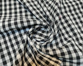 May include: Close-up of a black and white checkered fabric. The fabric is folded and draped, creating a swirling pattern. The pattern is a classic gingham design, with evenly spaced squares.