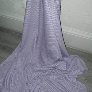 Può includere: Un rotolo di tessuto gingham bianco e viola. Il tessuto ha un piccolo motivo a quadri.