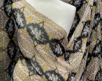 May include: Black sheer fabric with a gold and pink paisley pattern. The fabric is draped over a white dress form.