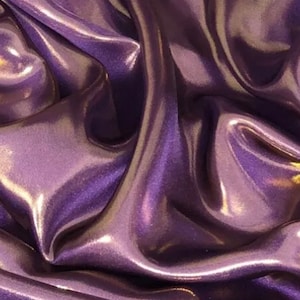 May include: Close-up of a smooth, iridescent purple fabric with a subtle sheen. The fabric is draped and folded, creating soft, flowing lines.