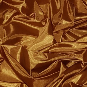 May include: A close-up of a golden brown satin fabric with a smooth, silky texture. The fabric is draped and folded, creating a luxurious and elegant look.