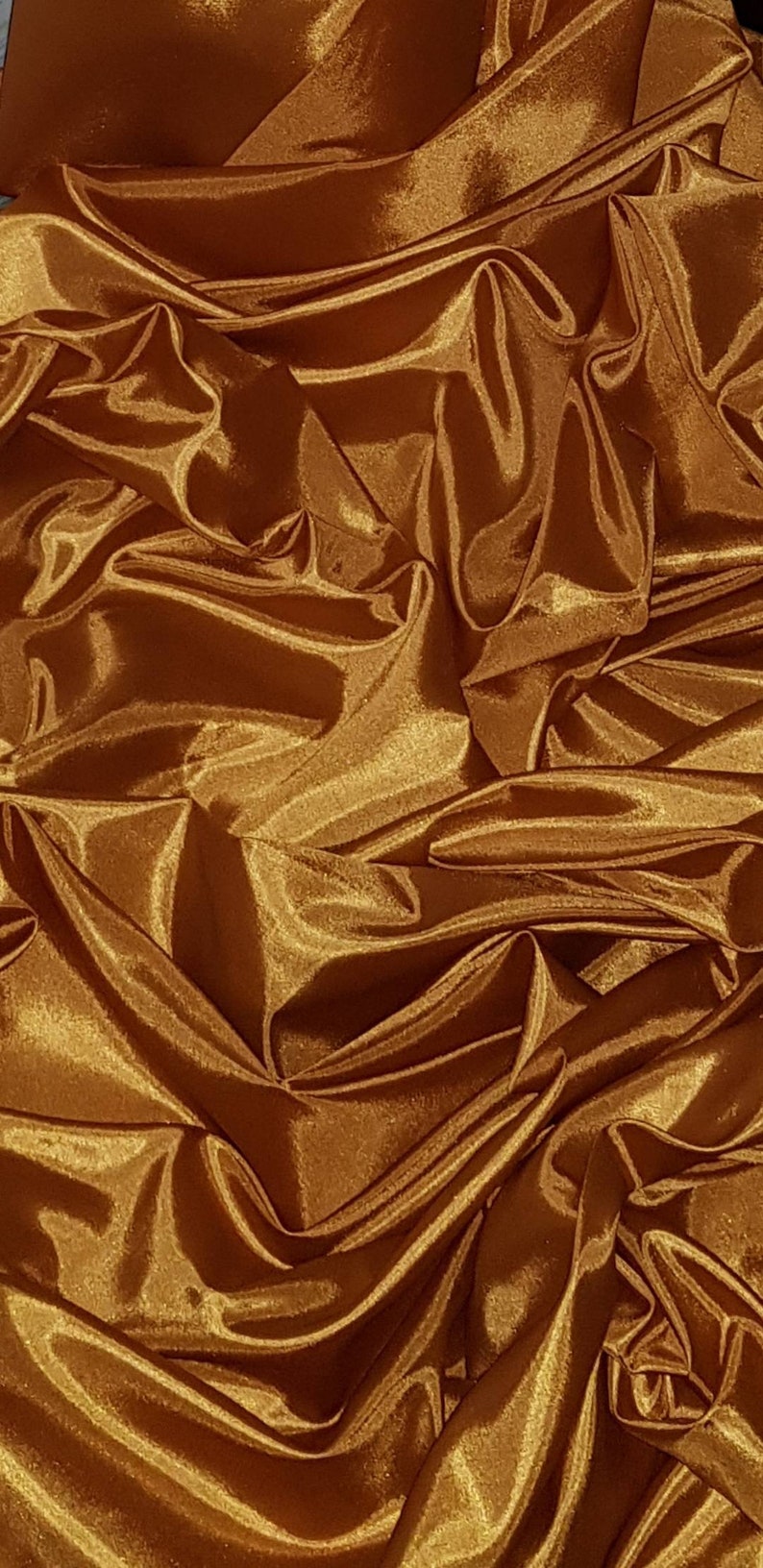 May include: A close-up of a golden brown satin fabric with a smooth, silky texture. The fabric is draped and folded, creating a luxurious and elegant look.