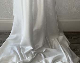 May include: A white satin fabric with a smooth, silky texture. The fabric is draped and folded, showcasing its luxurious feel.