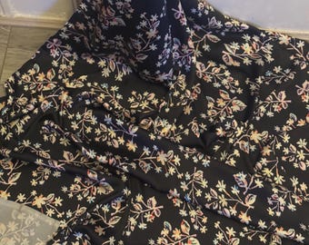 May include: Black fabric with a floral print in shades of pink, blue, and white. The fabric is soft and flowing, making it ideal for sewing dresses, skirts, or blouses.