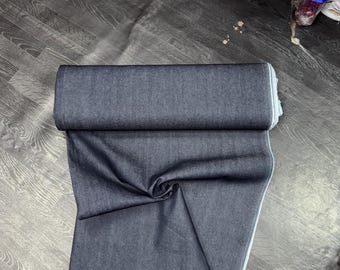 Op de afbeelding: Een rol donkerblauwe denim stof, gevouwen en gepresenteerd op een houten vloer.