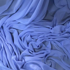 Pode incluir: Close-up de tecido azul claro fluindo. O tecido é drapeado e dobrado, criando ondas e sombras suaves. O material parece leve e transparente, com um brilho sutil.