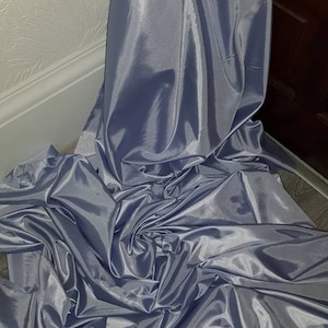 May include: A large piece of silver satin fabric, folded and draped on a light gray surface.