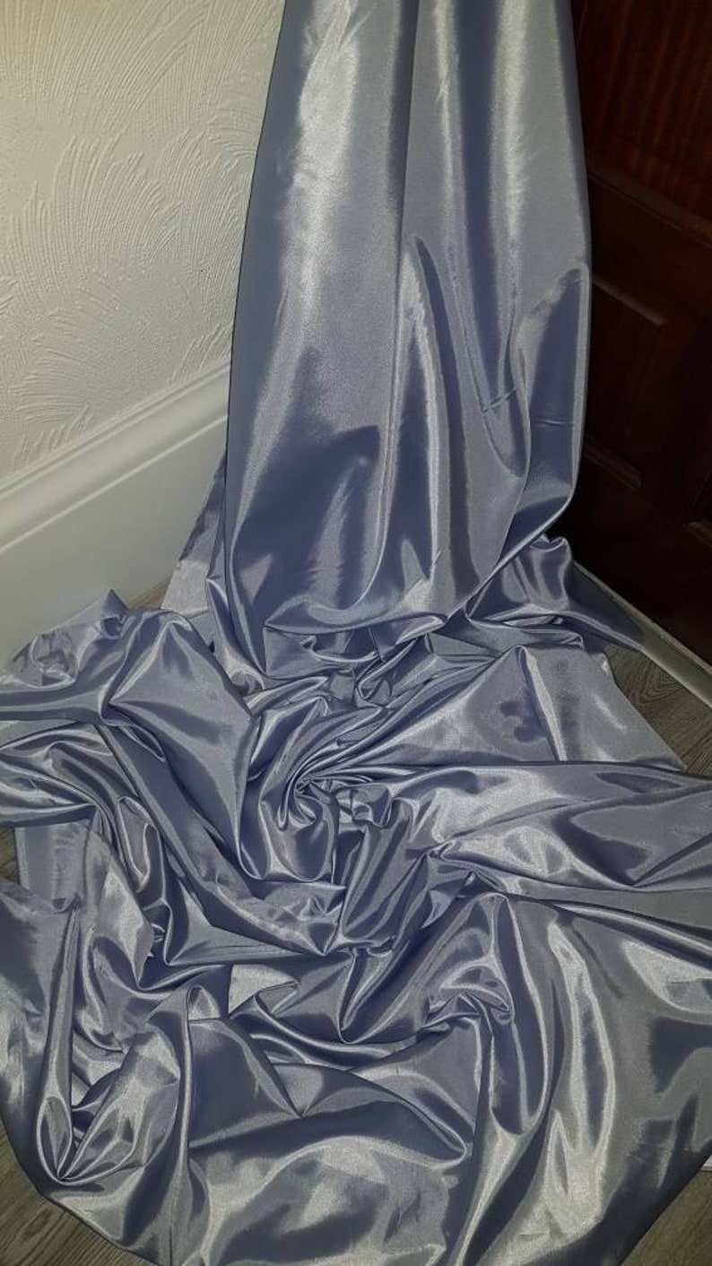 May include: A large piece of silver satin fabric, folded and draped on a light gray surface.