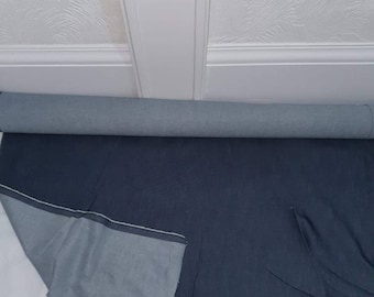 Op de afbeelding: Een rol donkerblauwe denimstof met een lichtere blauwe achterkant. De stof is uitgerold en toont de contrasterende kleuren en textuur. De stof is waarschijnlijk voor naai- of knutselprojecten.
