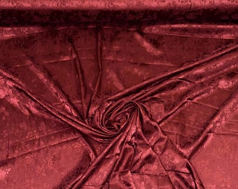 Peut inclure: Un rouleau de tissu rouge foncé avec un motif floral. Le tissu est drapé et plié, révélant le design et la texture complexes. La couleur est un rouge foncé riche, avec de subtiles variations de ton.