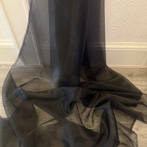 May include: Black sheer fabric, a lightweight and translucent material, draped and folded on a wooden surface.