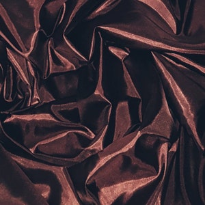 May include: Close-up of a deep burgundy satin fabric with soft folds and wrinkles. The fabric has a luxurious and elegant appearance.