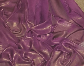 May include: Close-up of a draped fabric in shades of purple and gold. The fabric has a shimmering, metallic sheen, with soft folds and highlights. The material appears to be lightweight and flowing, suggesting it could be used for apparel or decorative purposes.