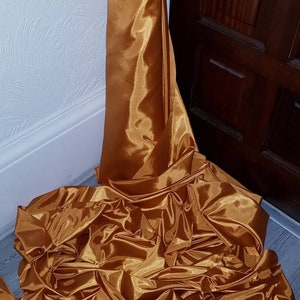 May include: A large piece of gold satin fabric draped and folded on a wooden floor.