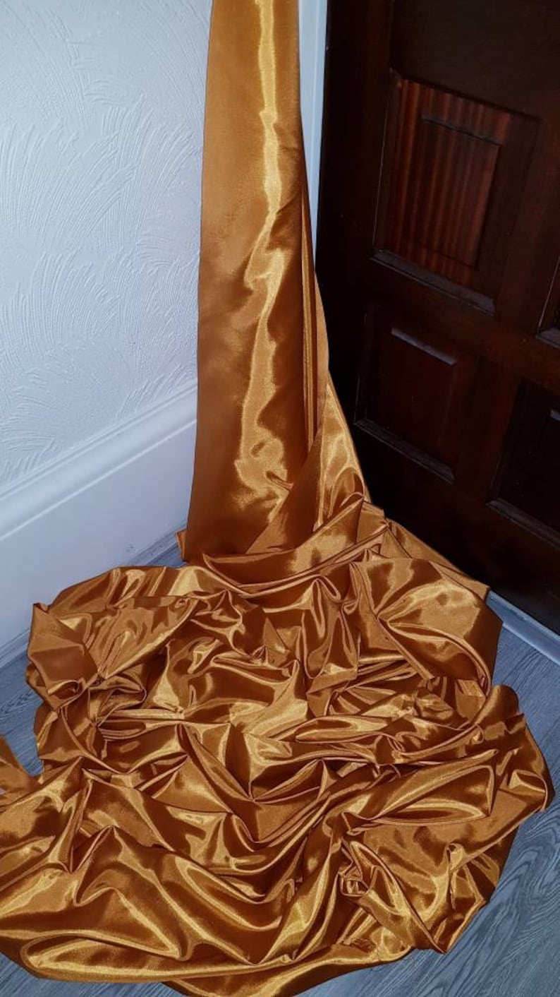 May include: A large piece of gold satin fabric draped and folded on a wooden floor.