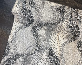 May include: A roll of fabric with a repeating pattern of black, gray, and white floral and dot designs. The fabric is rolled up, showing the edge of the material. The pattern includes small flowers and various sized dots.