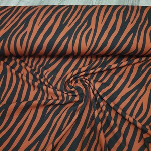Pu&ograve; includere: Un primo piano di un tessuto con una stampa a zebre nera e arancione. Il tessuto &egrave; piegato e drappeggiato, mostrando la trama e il motivo.