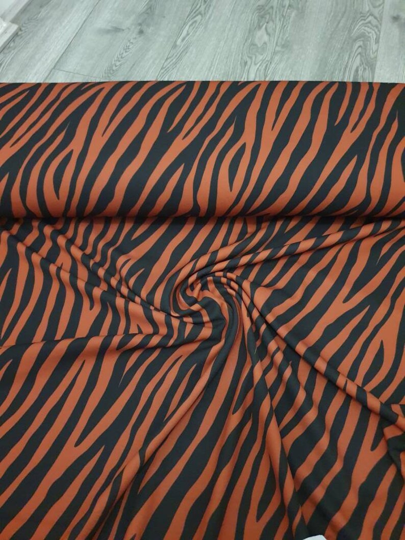Pu&ograve; includere: Un primo piano di un tessuto con una stampa a zebre nera e arancione. Il tessuto &egrave; piegato e drappeggiato, mostrando la trama e il motivo.
